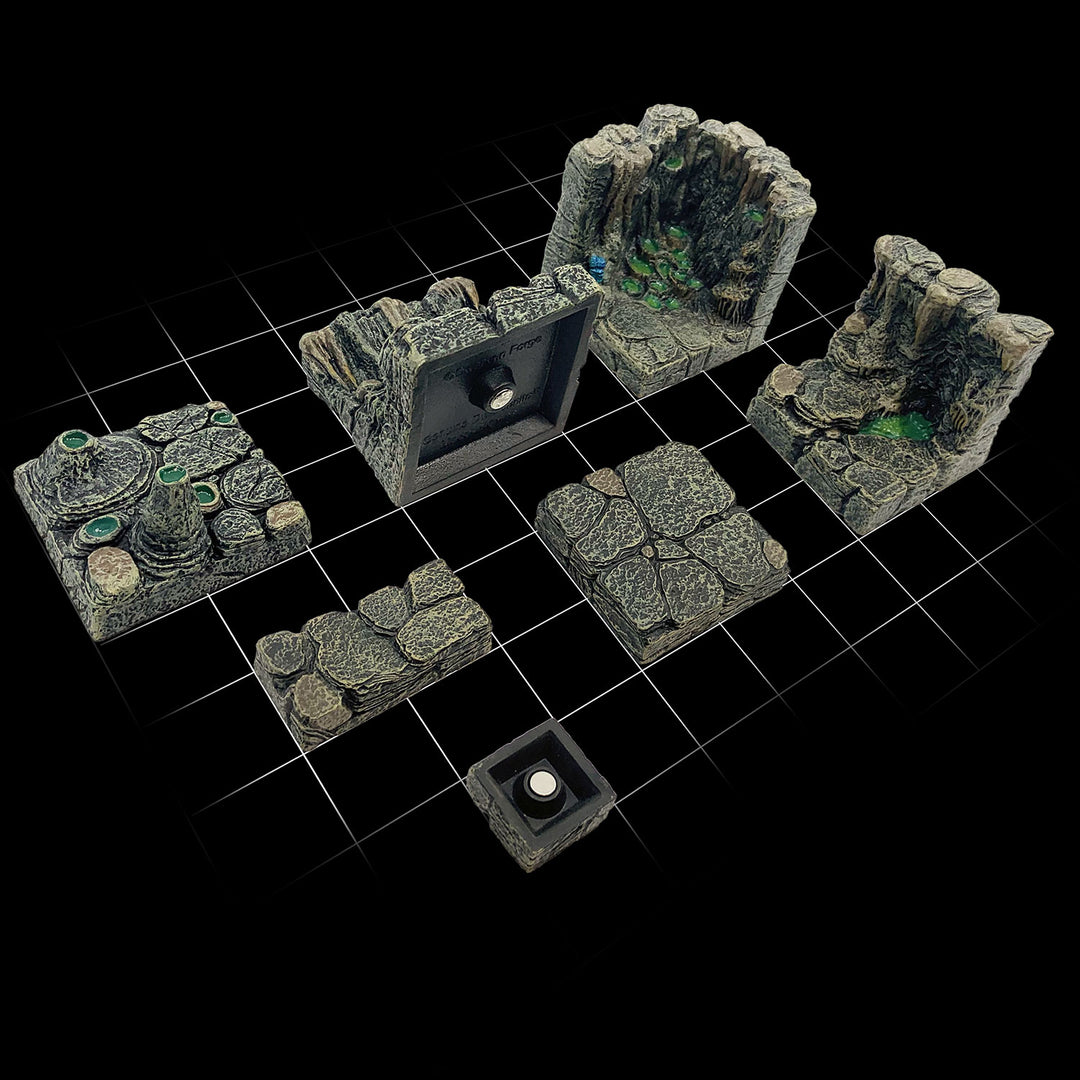 A 1-inch grid shown below various cavern wall and floor pieces to demonstrate the 1-inch grid integrated into each sculpt and anchor magnets at the bottom of each floor piece which affix to our metal terrain trays.